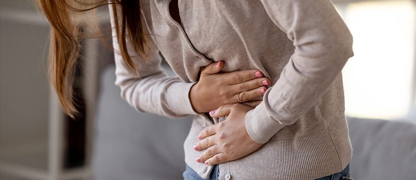 Mujer con dolor de estómago inclinada hacia adelante con las manos sobre la barriga.