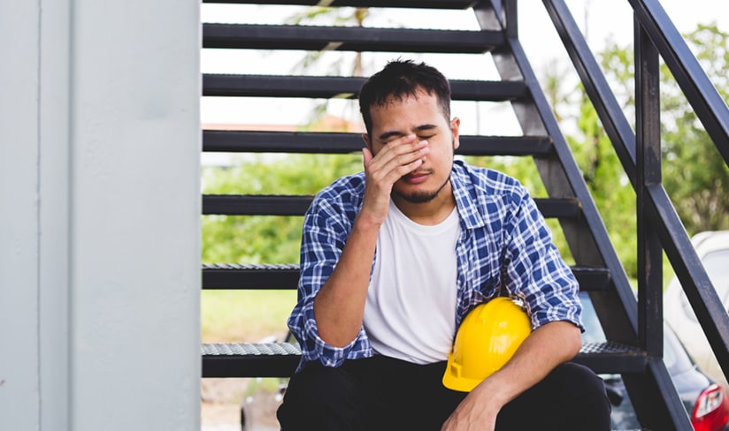 Trabajador de la construcción angustiado descansando en las escaleras con el casco en el regazo